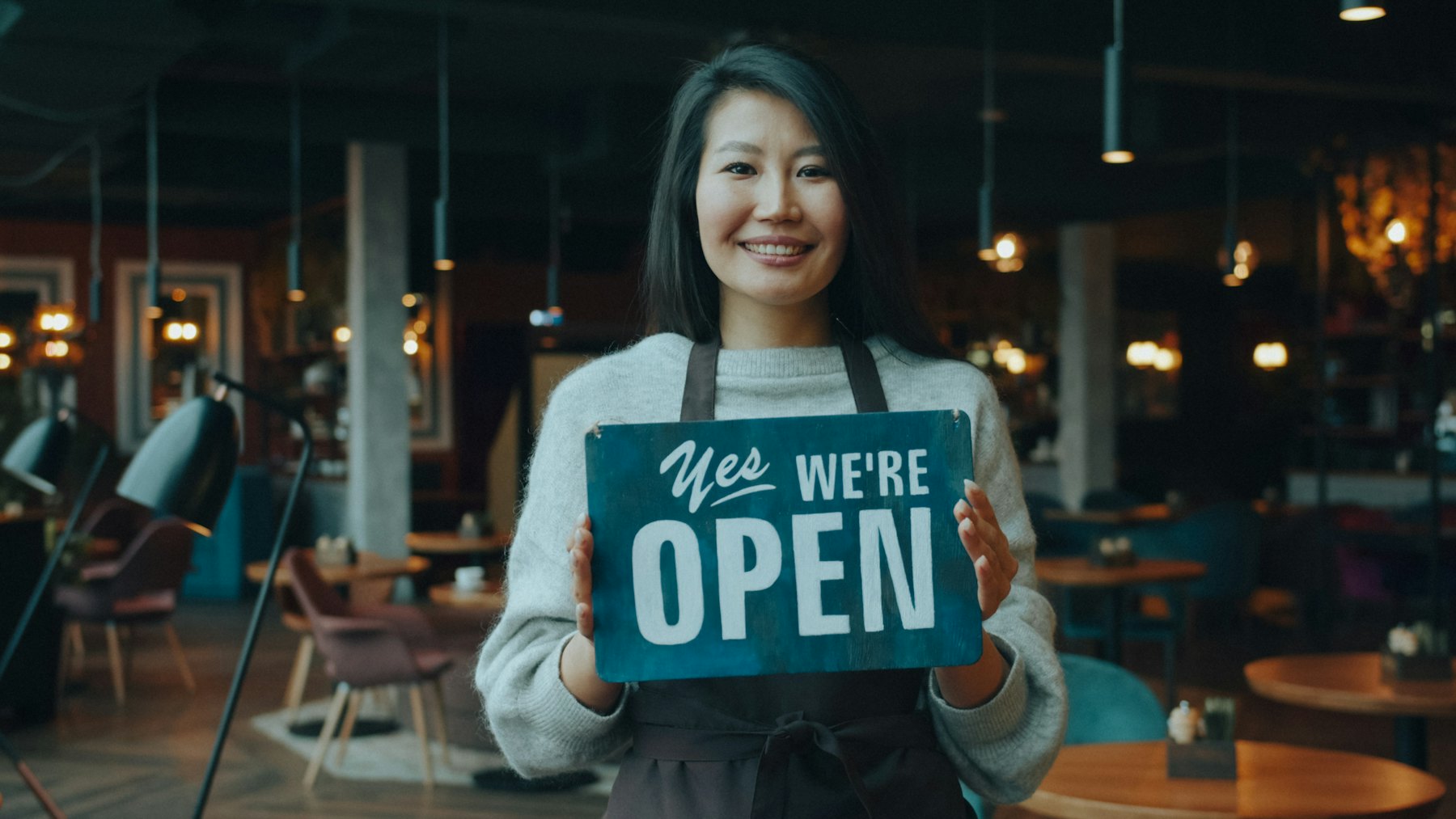 A café owner holding a sign that says Yes, we’re open
